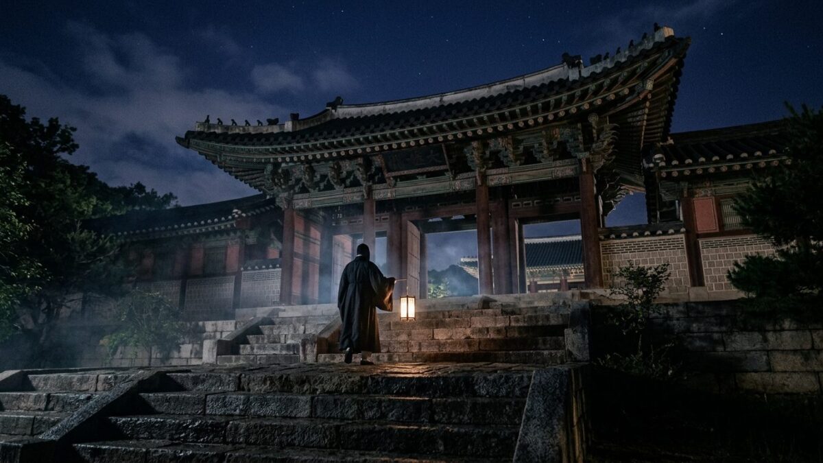 A lone figure with a paper lantern approaches a Joseon-era palace gate at night