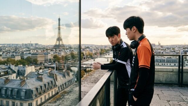Two esports players in team jackets with headsets stand on a Paris balcony overlooking the Eiffel Tower
