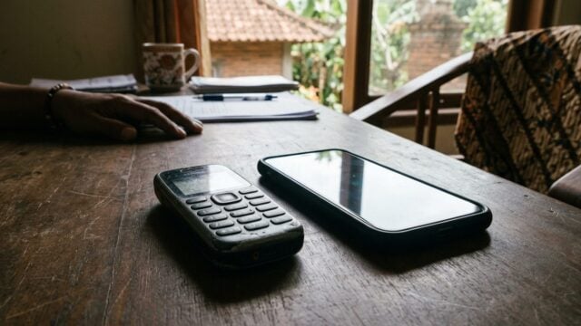 Seseorang memegang feature phone di samping ponsel pintar