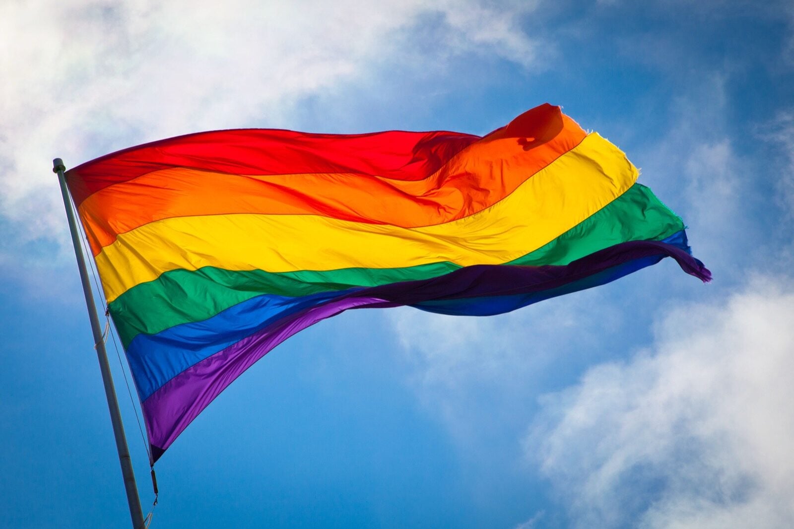 Rainbow Pride flag waving against a blue sky — LGBTQ+ symbol