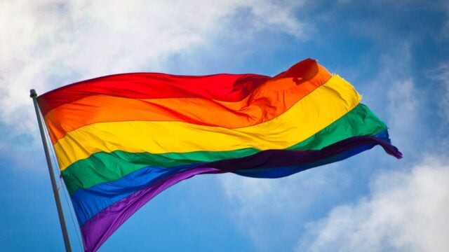 Bendera pelangi Pride berkibar di langit biru — simbol budaya LGBTQ+